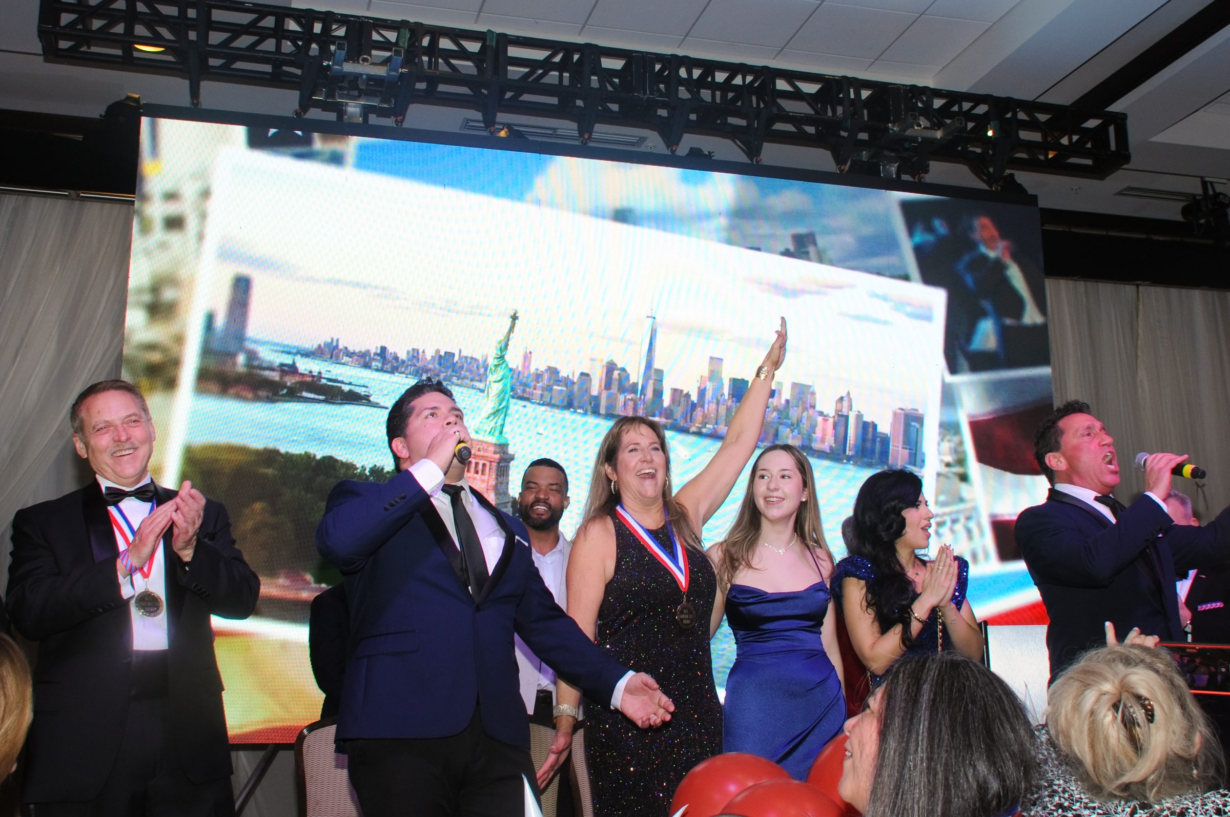 Patriotic celebration on stage with the New York skyline and Statue of Liberty projected behind cheering performers