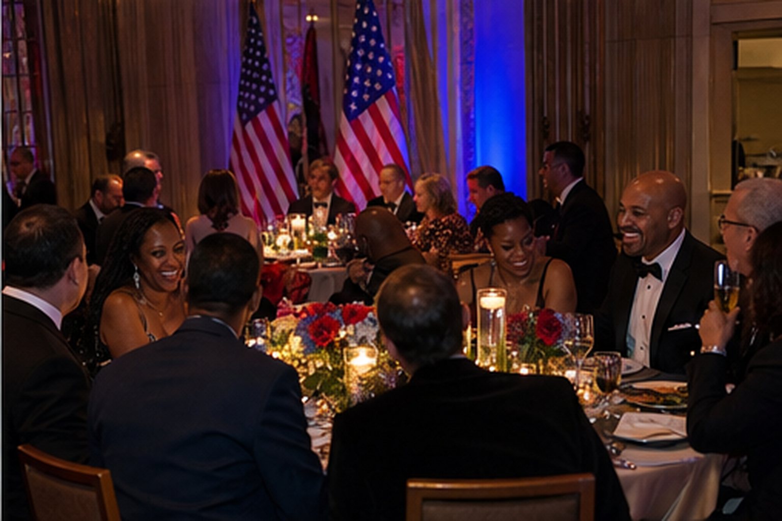 A Hosted Group seated together at their reserved round table inside the Statesman’s Concierge Area — American flags glowing on the back wall, candlelit dinner setting
