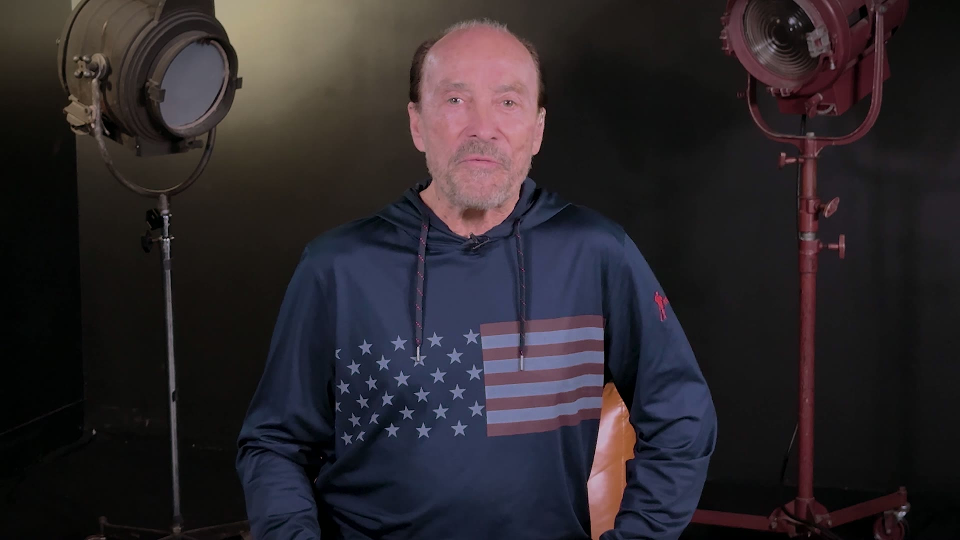 Lee Greenwood, in an American-flag hoodie, recording a video message for the Countdown 250 Ball